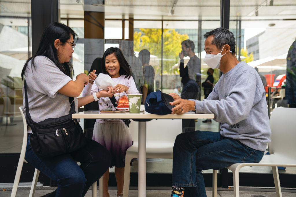 A family of three, including a child, are photographed sitting at a table in Cafe 5 enjoying a meal.